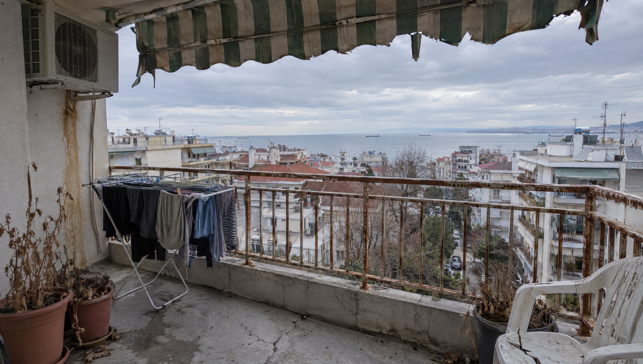Το ίδιο μπαλκόνι πριν, με σκουριασμένα κάγκελα, σκισμένη τέντα και απλώστρα