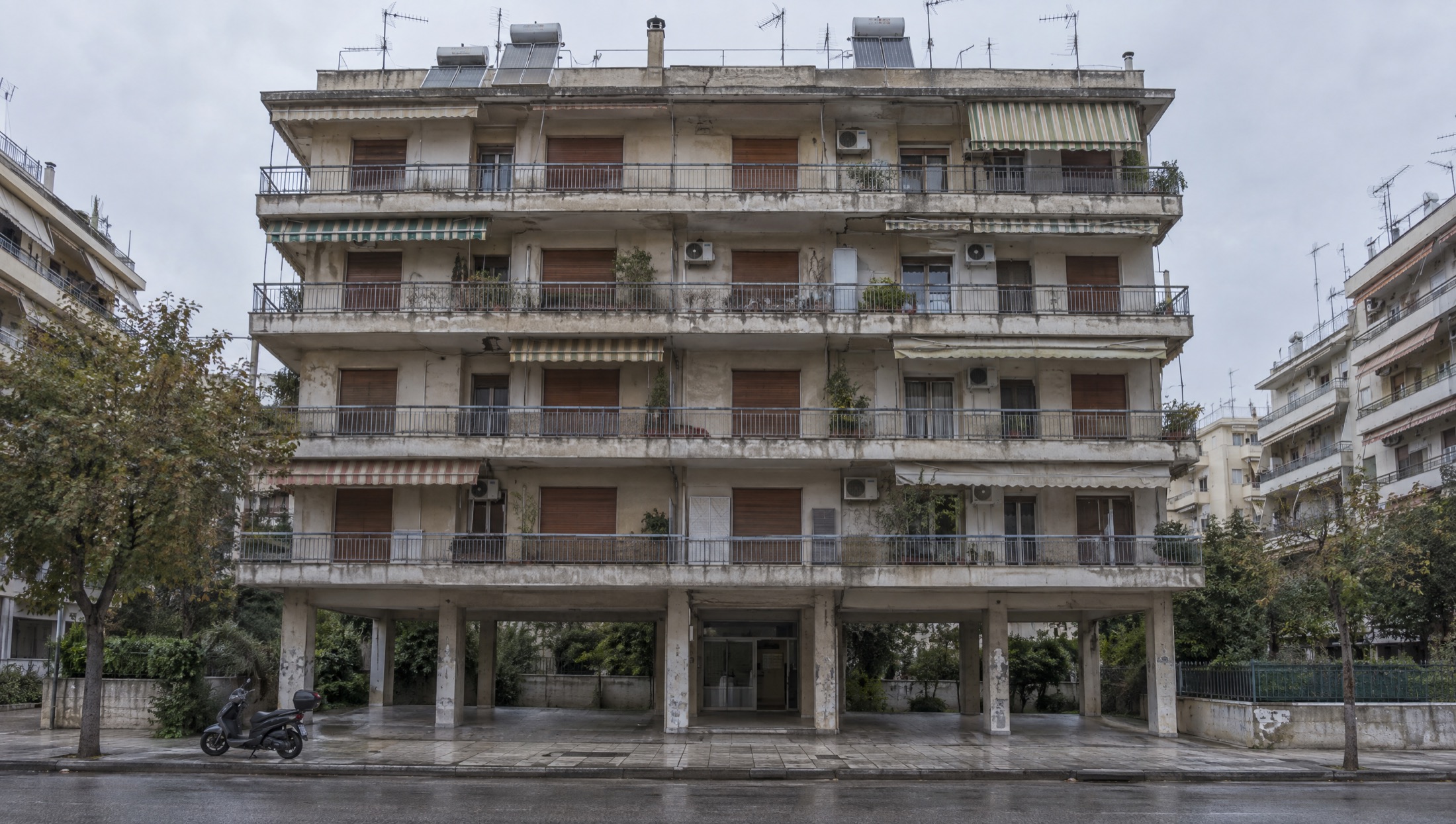 Η ίδια πολυκατοικία πριν, με λεκιασμένο μπετό, σκισμένες τέντες και κλιματιστικά