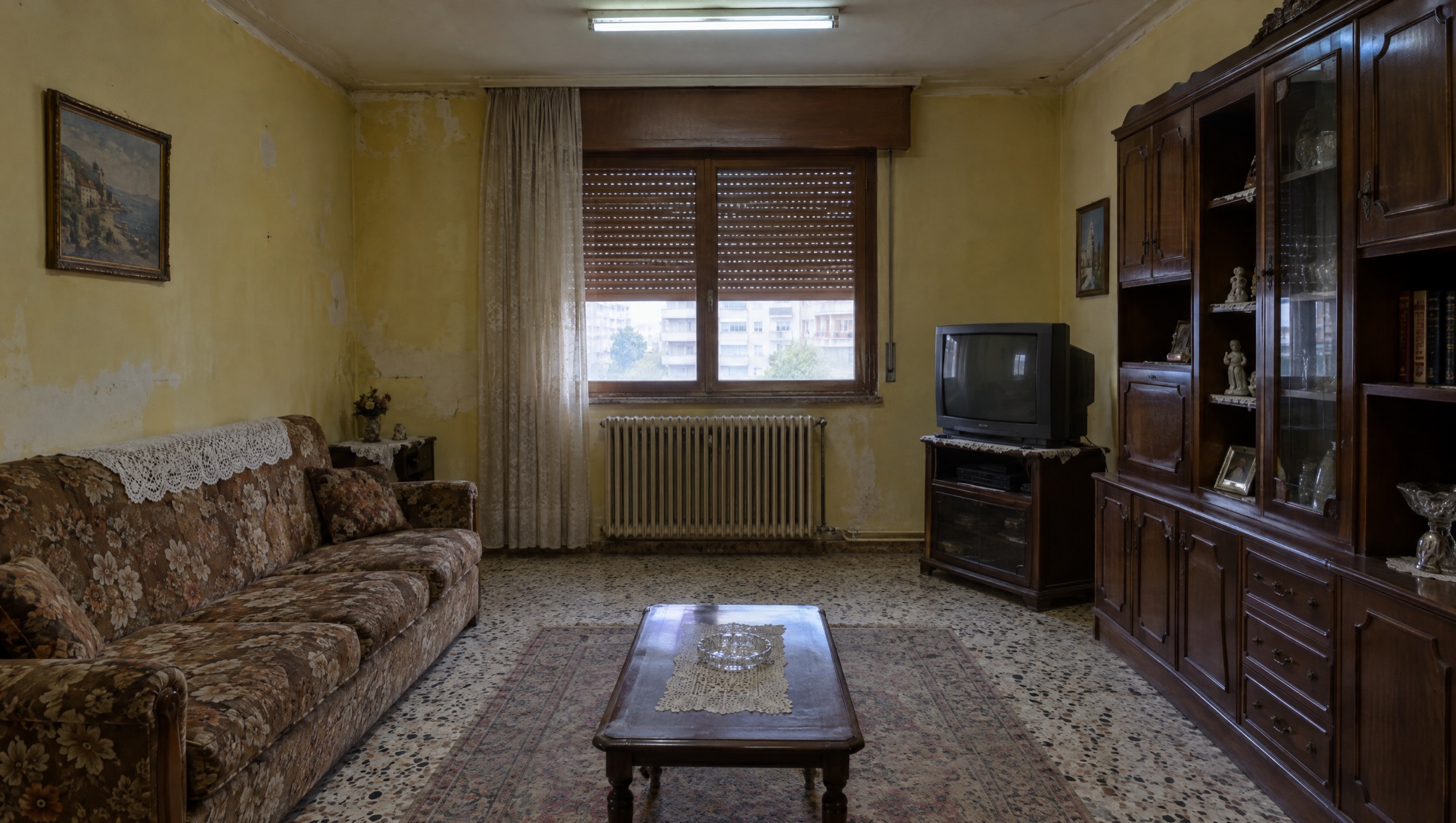 Το ίδιο σαλόνι πριν, με κιτρινισμένους τοίχους, λουλουδάτο καναπέ και ρολά